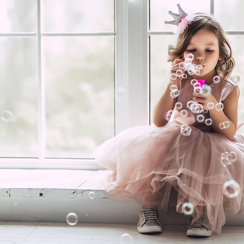 Petite fille habillée en princesse soufflant des bulles